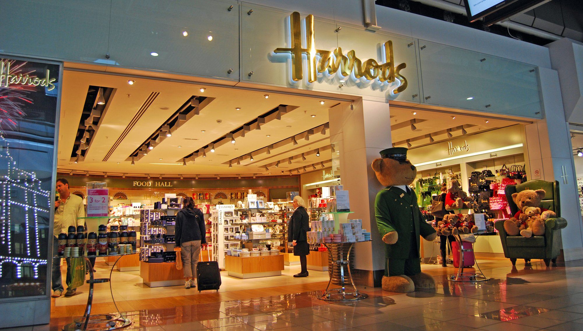 A Harrods store at Heathrow airport, with its gold sign and a doorman bear at the entrance.
