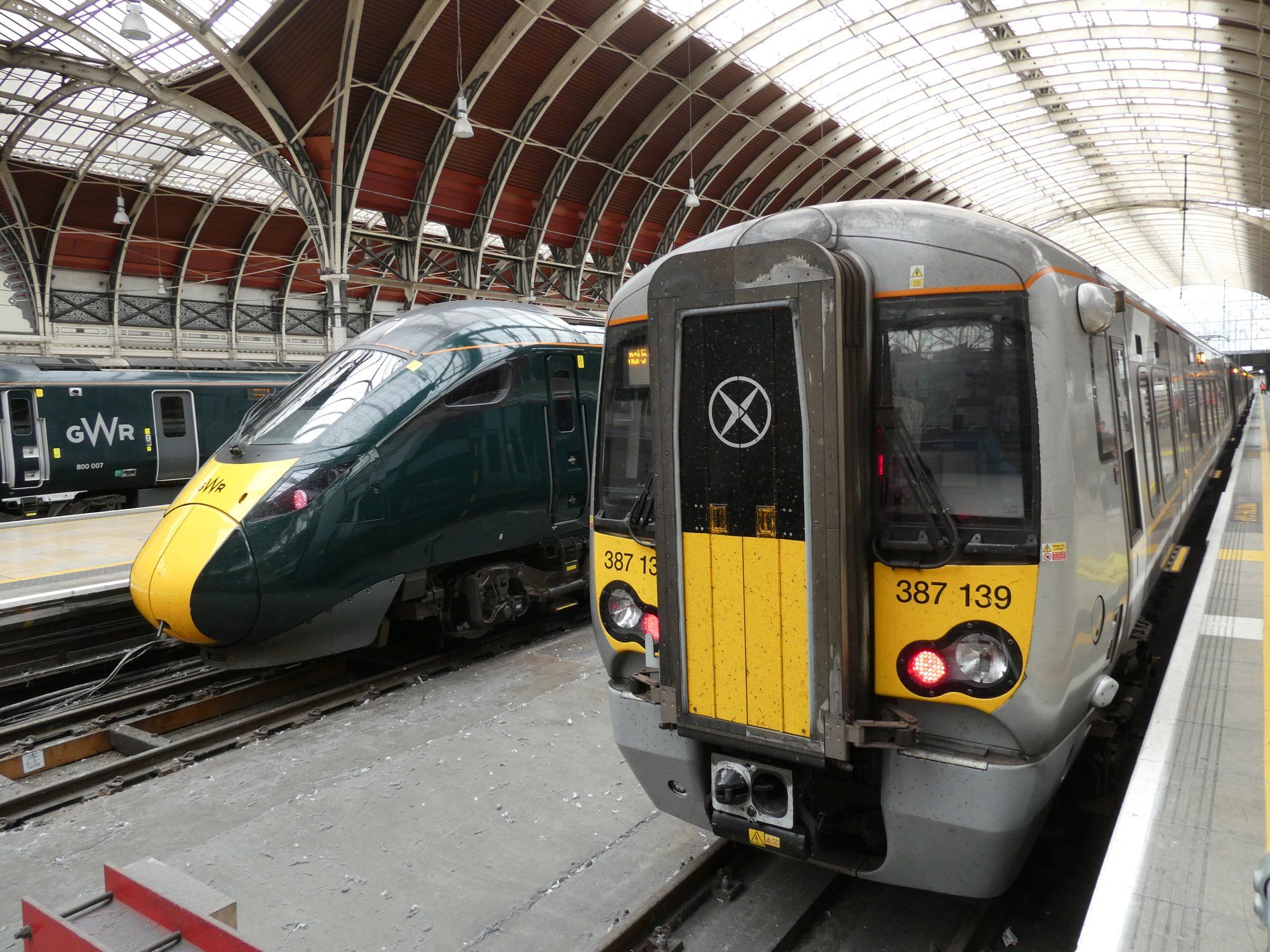 A purple and white Heathrow Express Class 387 train at London Paddington station, beside a Great Western train.