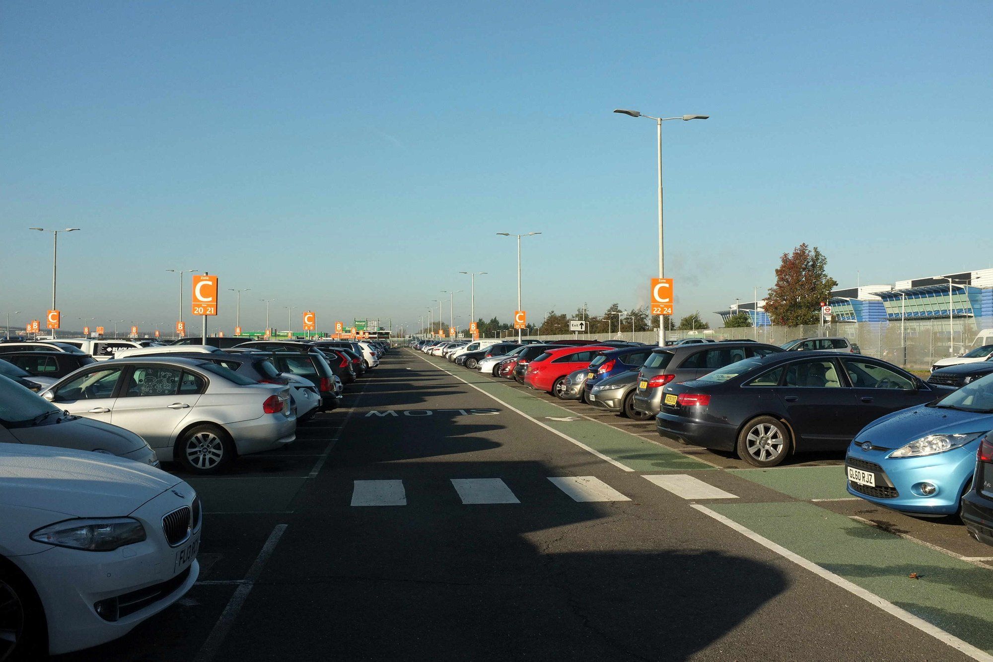 Rows of cars in an open-air Heathrow car park, with orange zone marker signs.