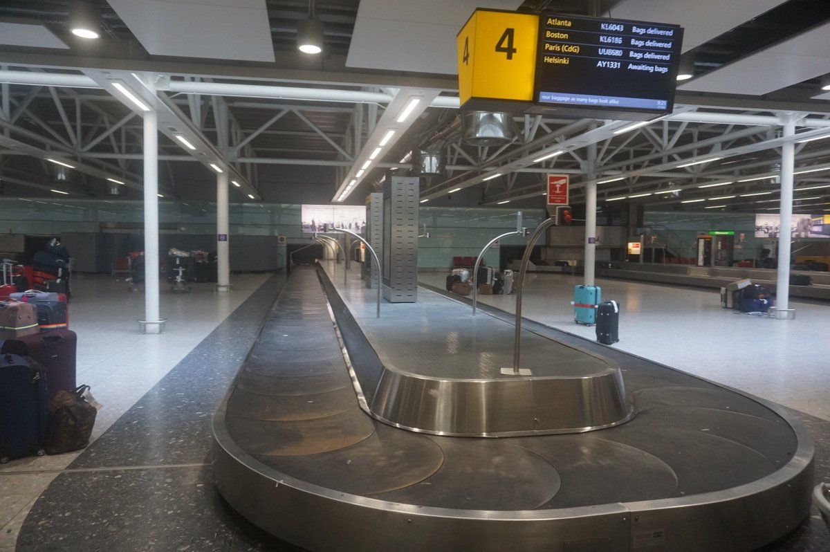A baggage reclaim carousel at Heathrow Terminal 3, with a flight information board above showing arriving flights.