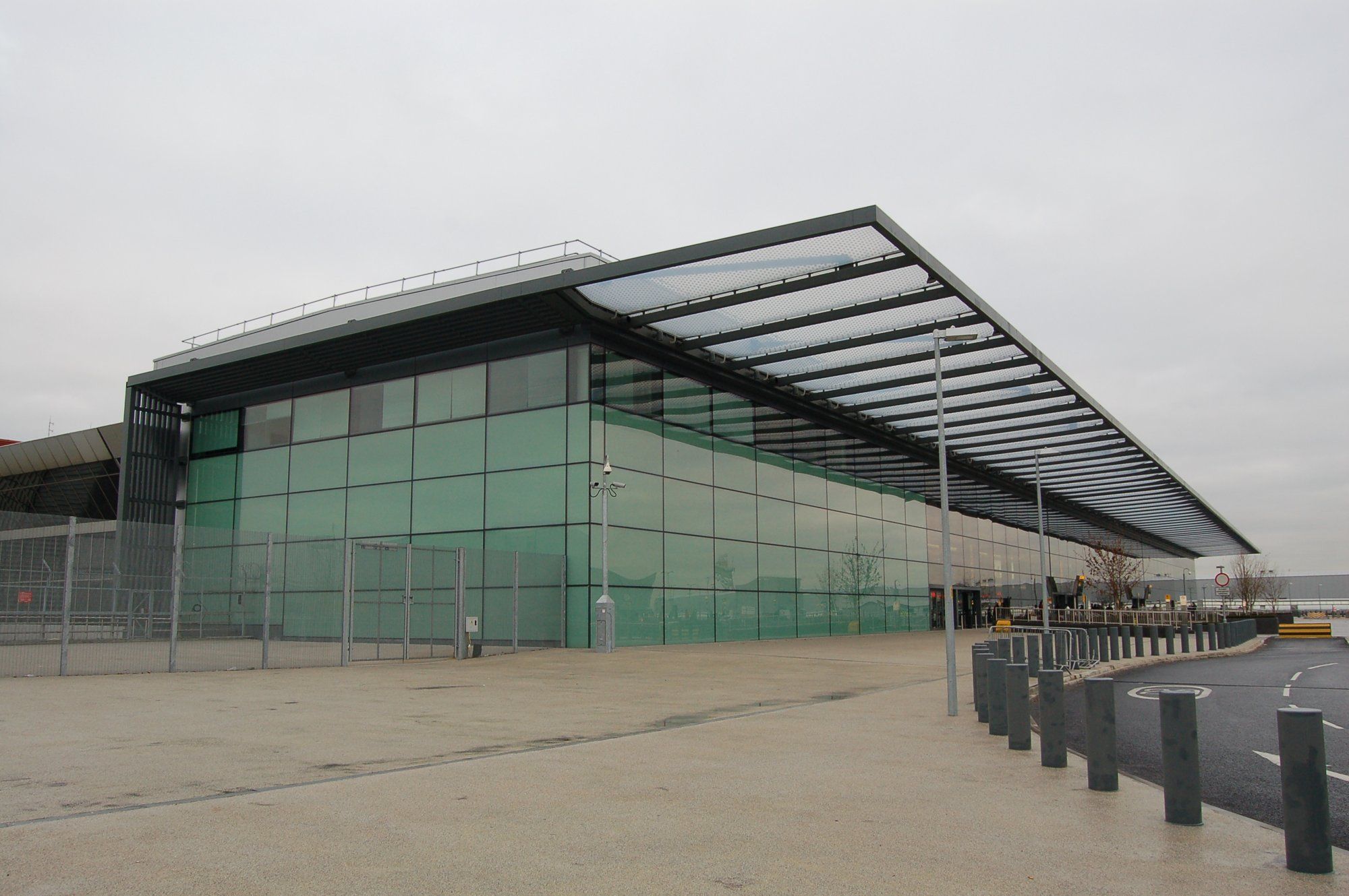 The green-glass frontage of the Heathrow Terminal 4 building, with its long canopy roof, on an overcast day.